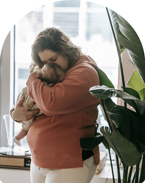 Madre abrazando a su bebé junto a una ventana
